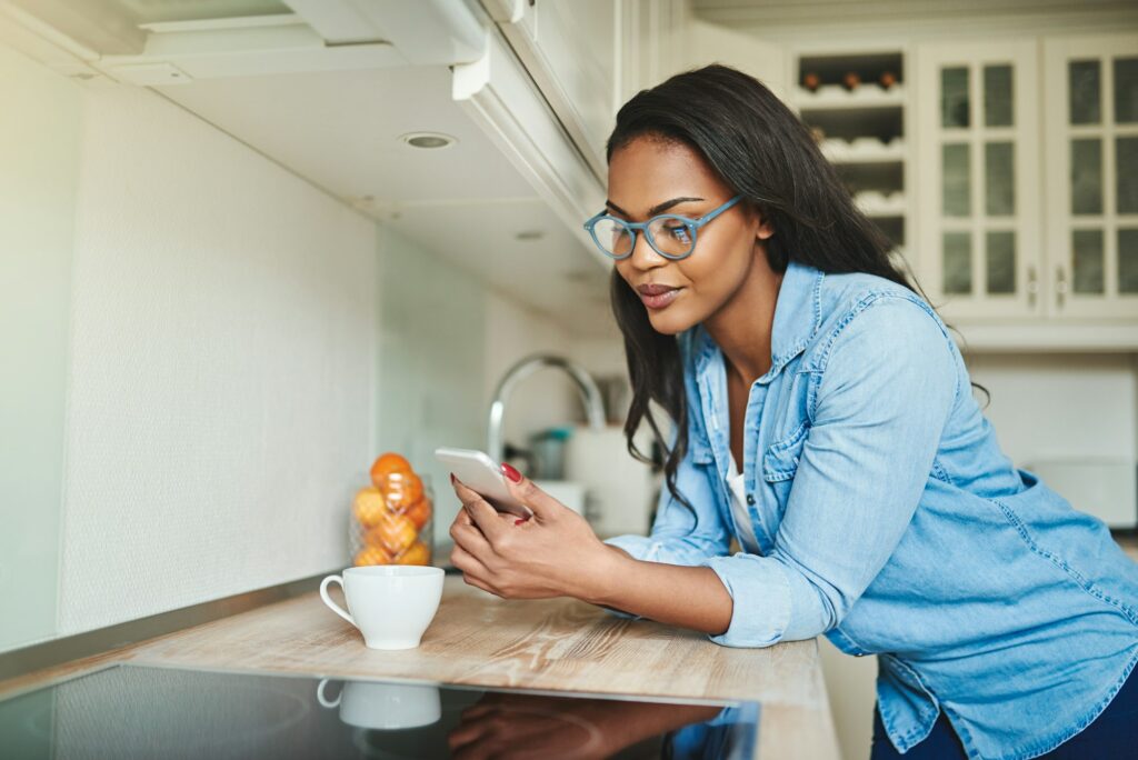 Young African woman drinking coffee and texting on a cellphone